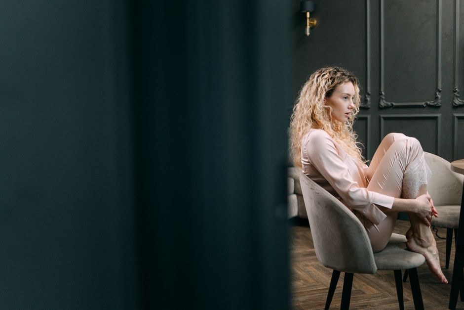 A woman in loungewear sits thoughtfully in a stylish, dimly lit room.