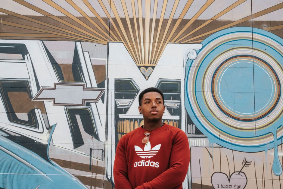 Young man in red Adidas shirt posing by colorful street art mural in Richmond, VA.