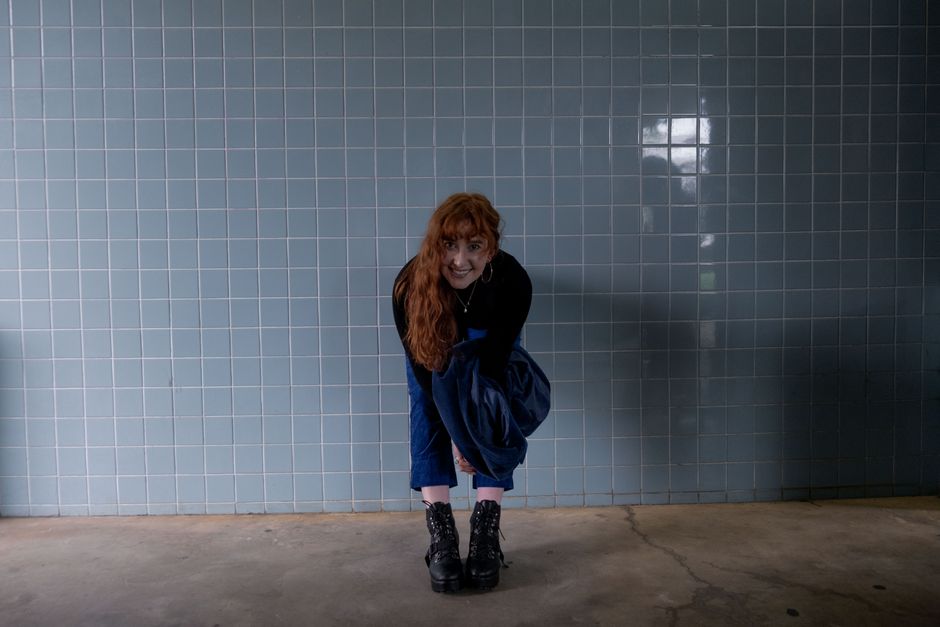 A fashionable woman smiling against a tiled wall, expressing style and modern fashion.