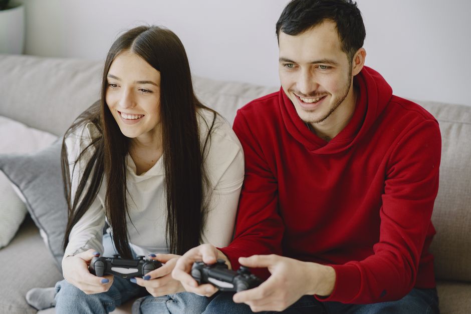 Happy couple enjoying video games together, sitting on couch indoors with controllers.