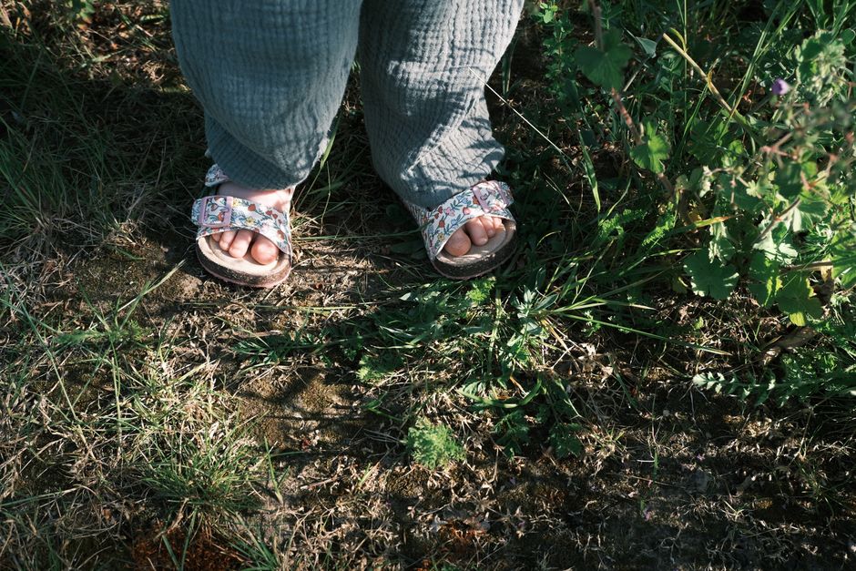 Close-up of a child's feet wearing floral sandals standing on green grass outdoors.