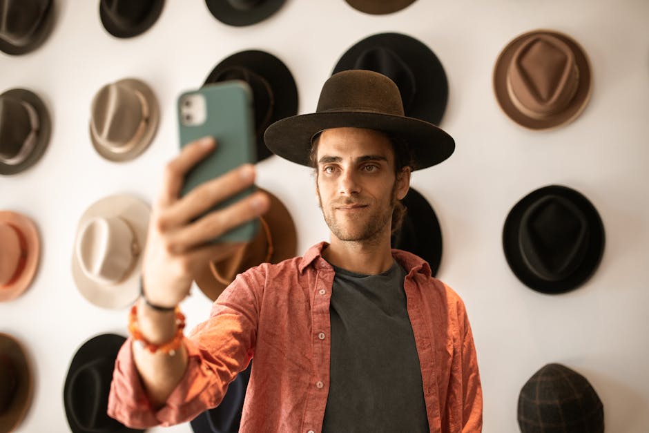 A fashionable man takes a selfie in a trendy hat store with a variety of hats displayed behind him.
