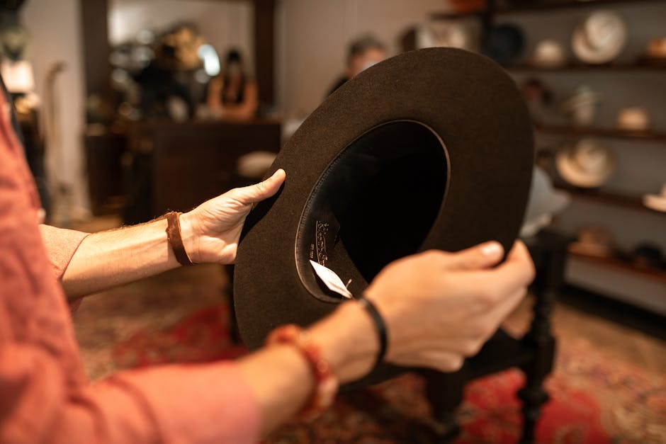 Close-up of hands holding a black fedora hat in a hat store interior.