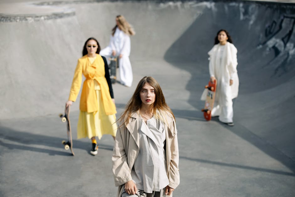 Stylish women in long dresses and coats pose in a modern skate park setting with skateboards.