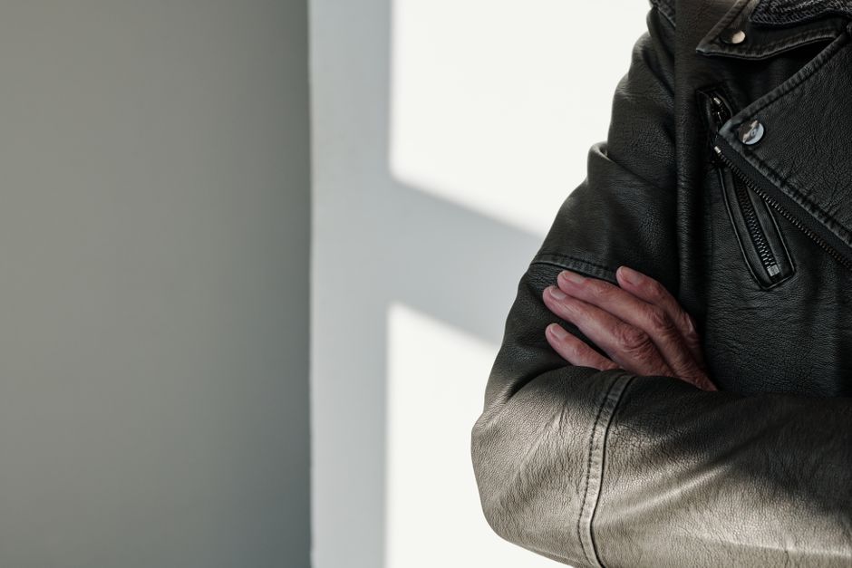 Close-up of crossed arms in a black leather jacket with sunlight casting shadows.