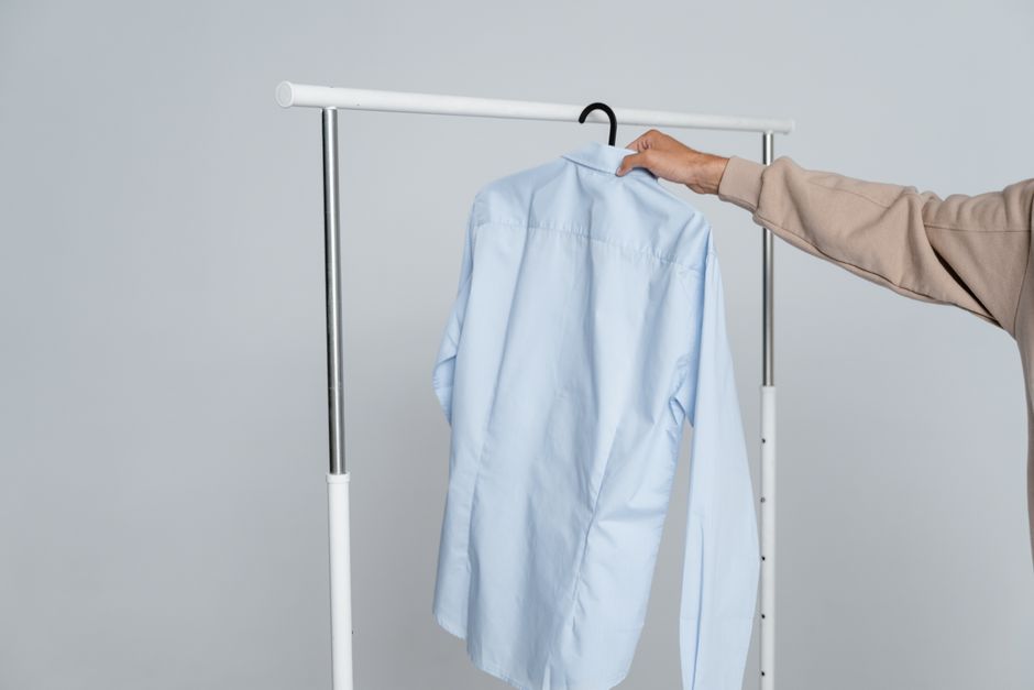 A person holding a blue shirt on a rack against a neutral background.
