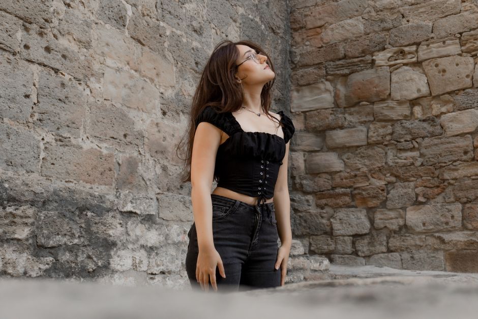 A young woman in a stylish black outfit posing against an ancient stone wall in Baku, Azerbaijan.