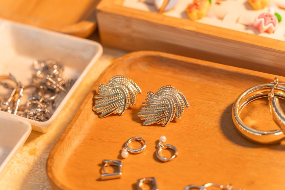 A close-up of elegant silver earrings and rings displayed on a wooden tray with warm lighting.