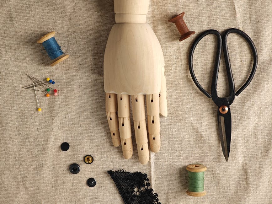 Flat lay of sewing tools and wooden mannequin hand on linen fabric.