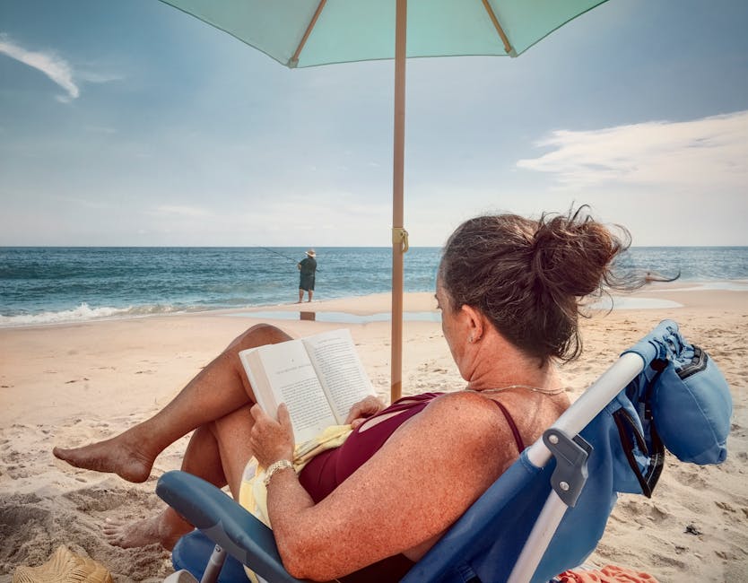 A woman reading a book under an umbrella on a peaceful beach, enjoying summer vibes.