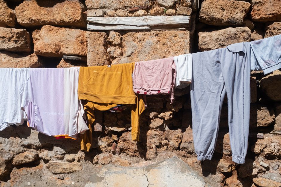 Colorful clothes hanging on a line against a rustic stone wall in sunlight.
