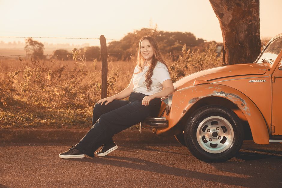A woman sitting on an orange vintage Beetle car during a warm sunset outdoors.