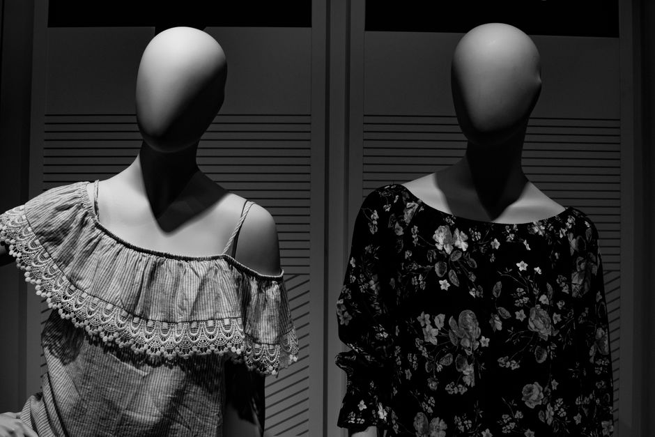 Black and white mannequins in feminine elegant dresses placed in showcase in clothing store