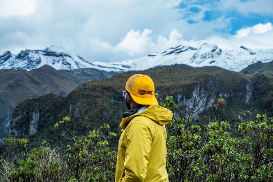 A man stands outdoors in a yellow jacket and cap, gazing at snow-capped mountains, showcasing nature's beauty.