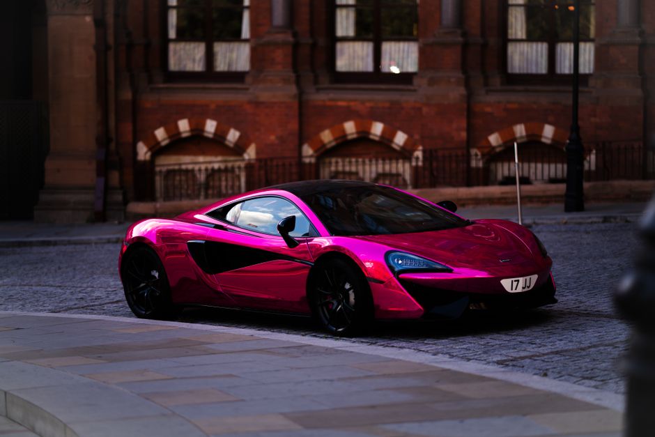 A shiny red sports car parked on a cobblestone street in London, with historic architecture in the background.