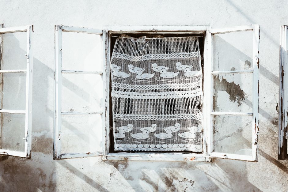 Rustic open window with a white lace curtain featuring duck motifs.