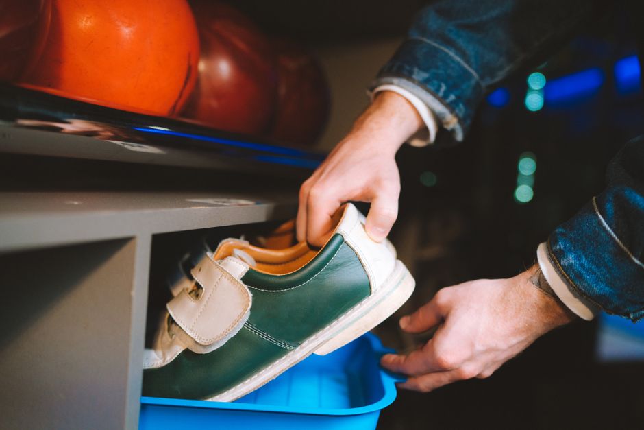 Close-up of hands handling bowling shoes with bowling balls in the background.