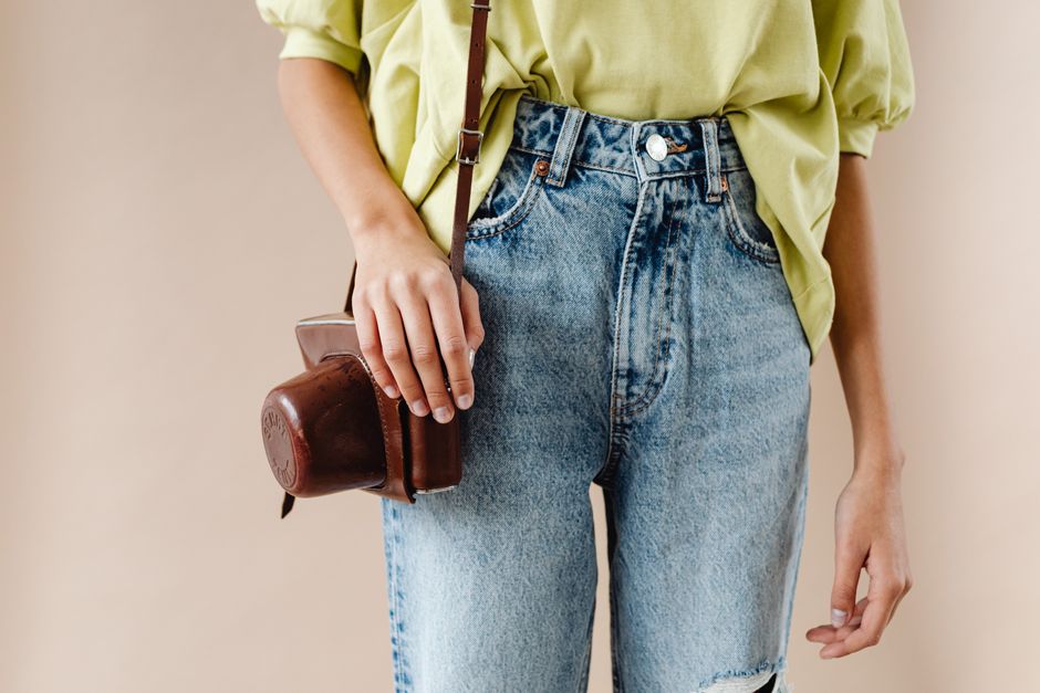 A stylish person in jeans holds a vintage camera, showcasing casual fashion.