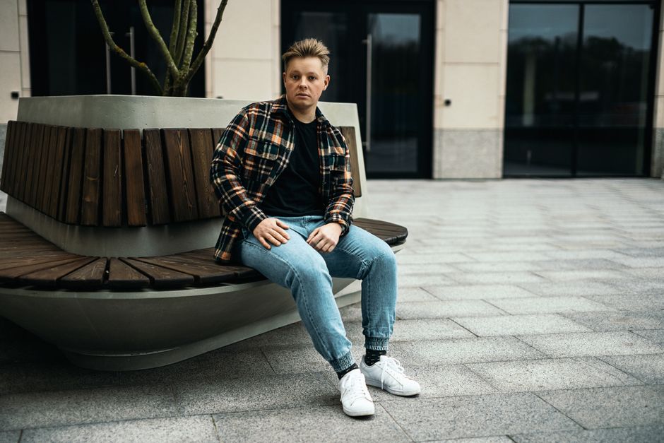 Young man in casual attire sitting on an outdoor bench in Minsk, showcasing relaxed fashion style.