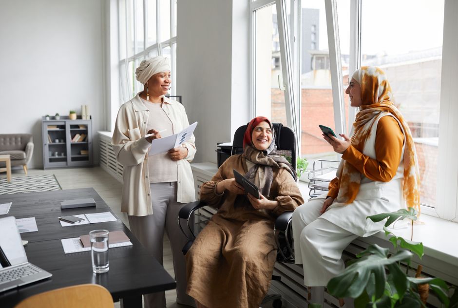 Three diverse women engaging in a collaborative office meeting, showcasing teamwork and joy.