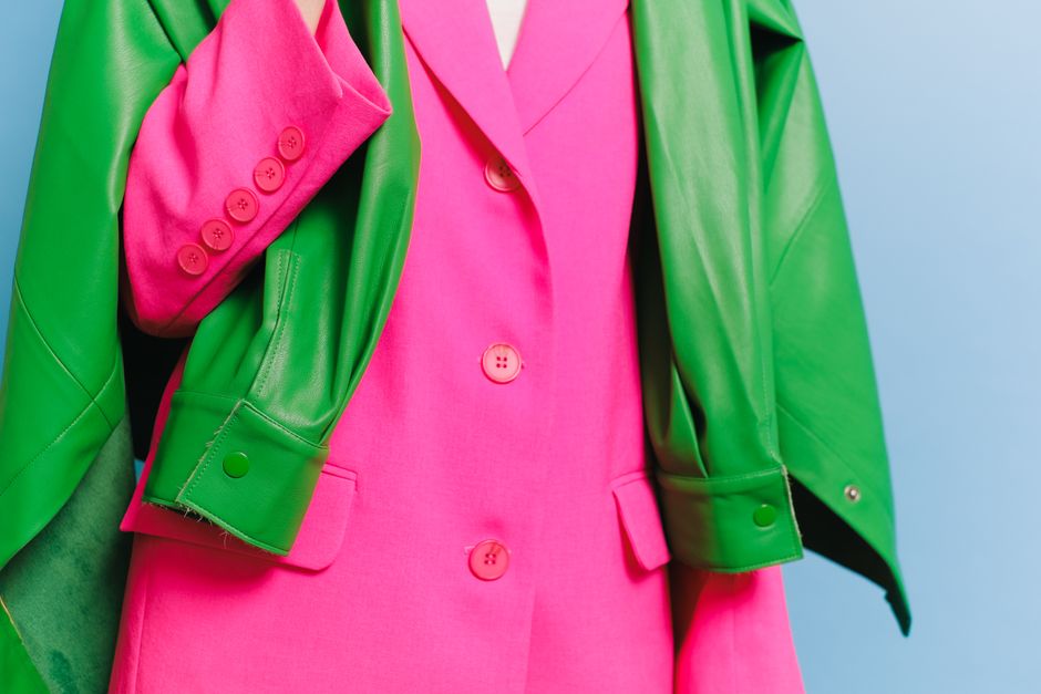 Stylish pink blazer with a contrasting green leather jacket draped over it, showcasing bold fashion colors.