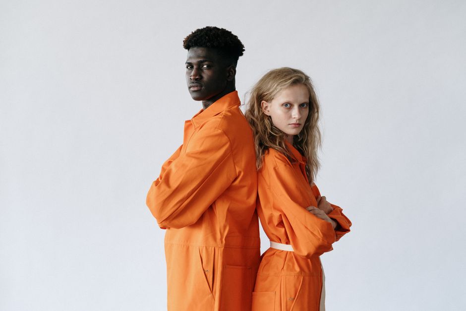 Two adults standing back-to-back in vibrant orange uniforms on a white background.