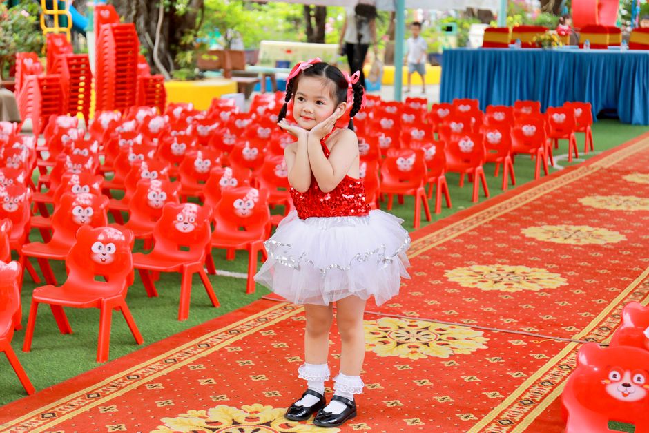 A young girl in a red and white costume at an outdoor event with vibrant chairs.