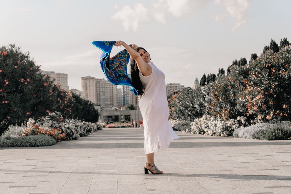 A joyful woman in a white dress dances with a scarf in a sunny park setting.