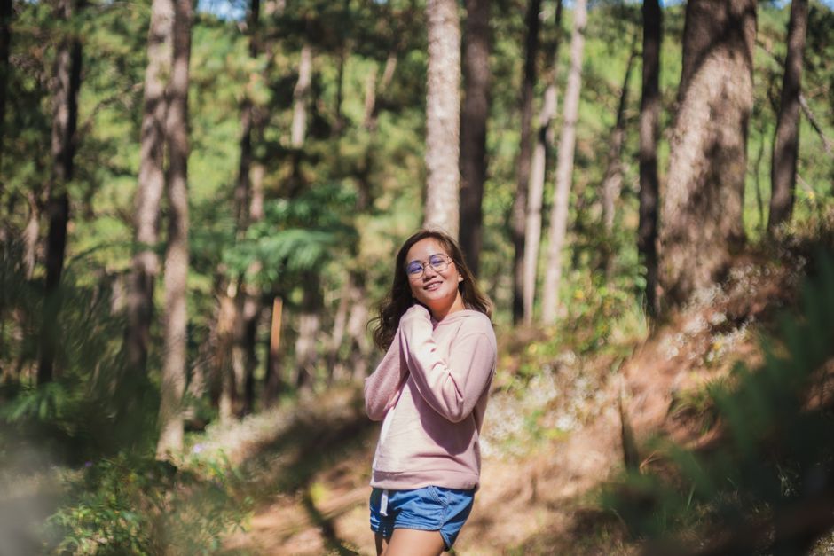 Happy young slim female in shorts and shirt with long sleeves looking away with bright smile and hands folded under chin in summertime on blurred background