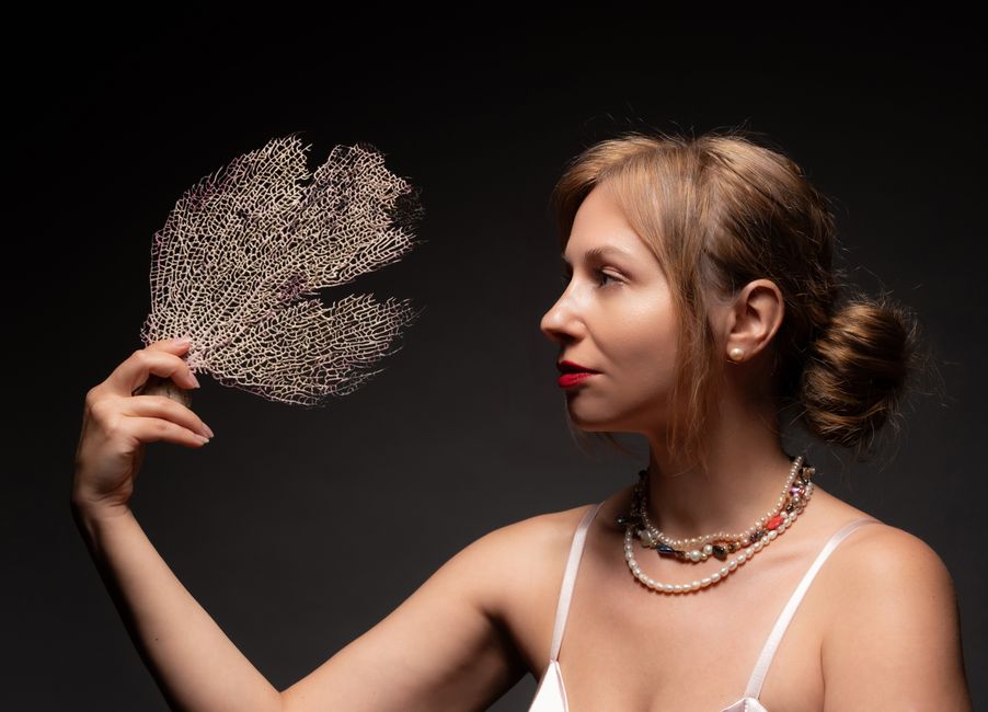 A woman elegantly holding a sea fan coral in profile view. Studio lighting.