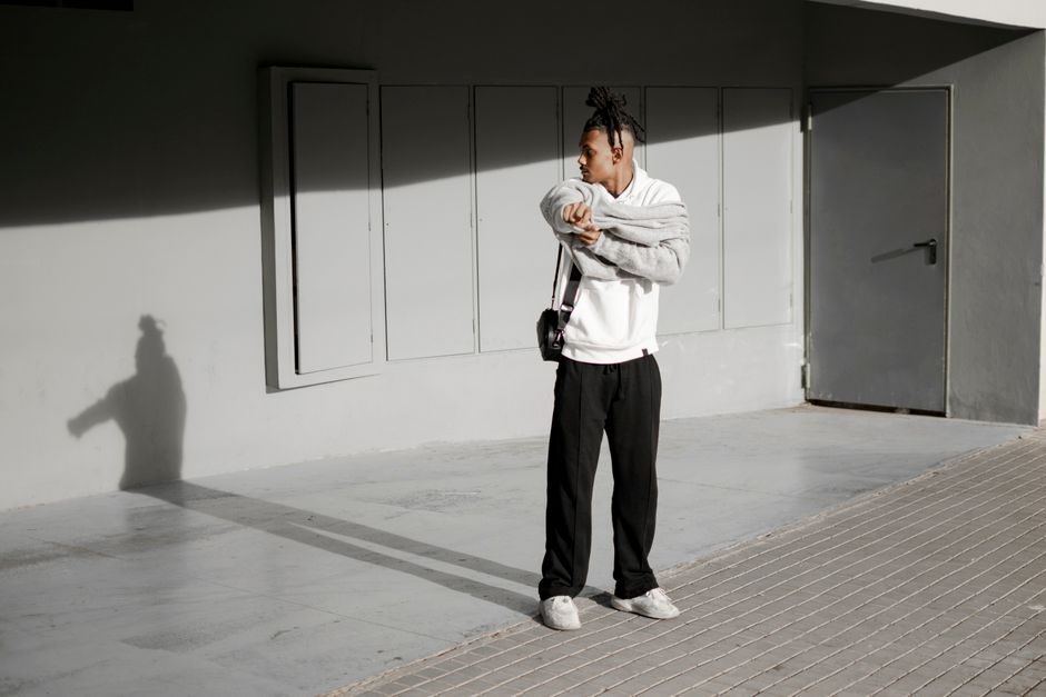 Stylish man with dreadlocks standing outside, casting a shadow on the wall.