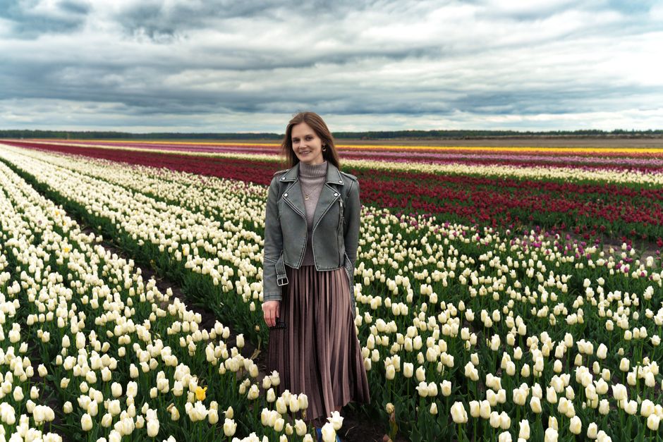 A woman stands amidst vibrant tulip rows under a cloudy sky, showcasing spring florals.