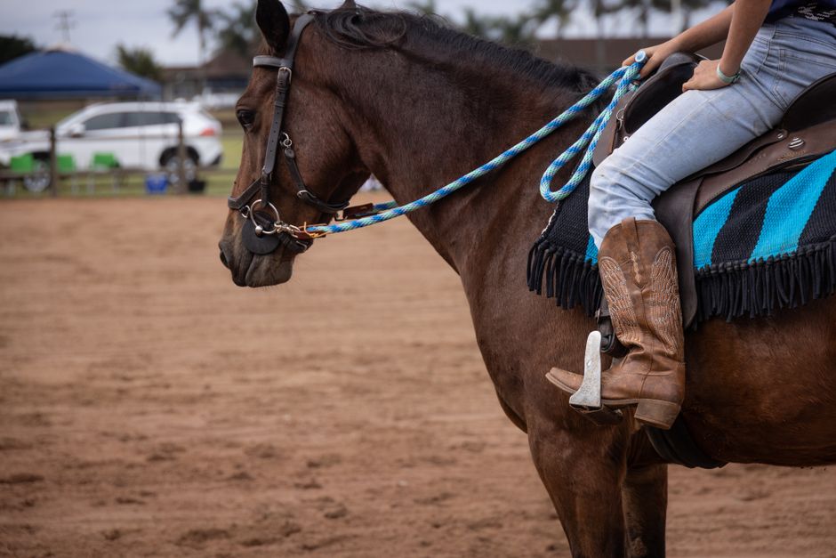 Close-up of a horse and rider in cowboy boots during an equestrian event outdoors.