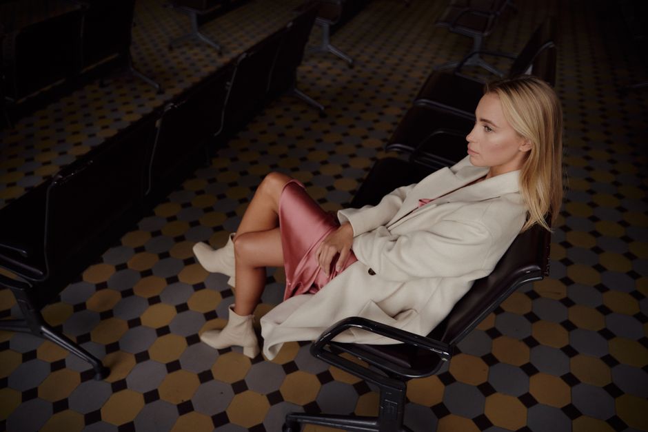 A fashionable woman in a beige jacket sitting indoors, exuding elegance and style.