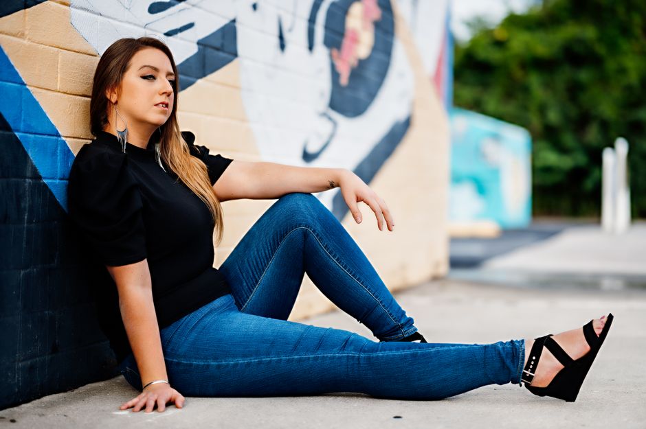 Stylish woman in denim and black shirt posing by graffiti wall in urban Orlando.