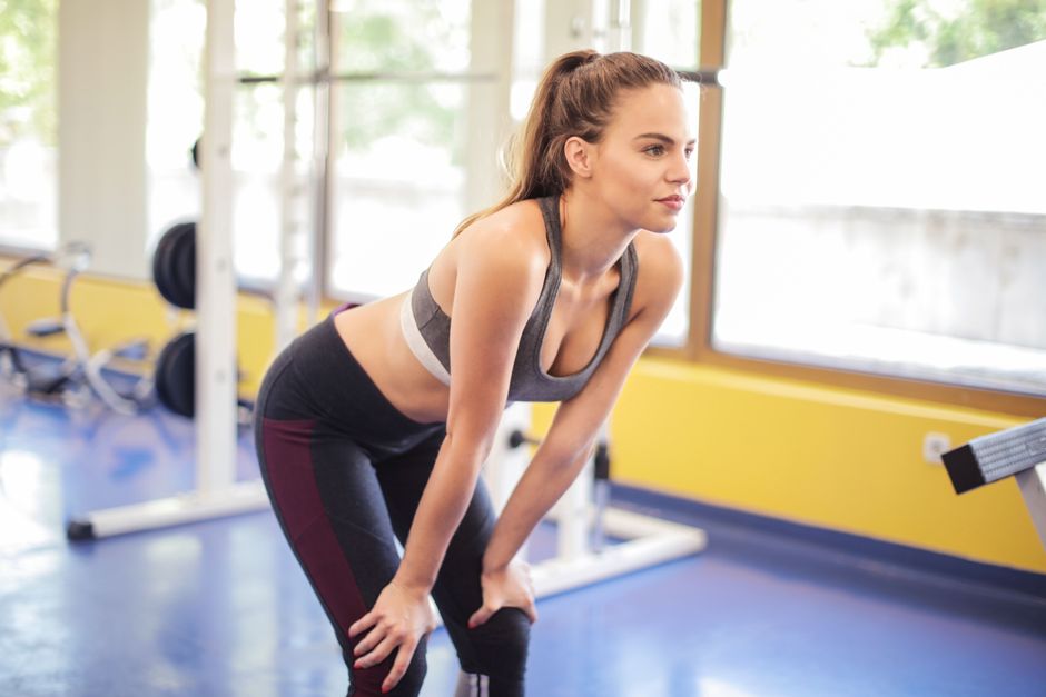 Fit woman performing a stretch indoors, showcasing fitness and active wear in a modern gym environment.