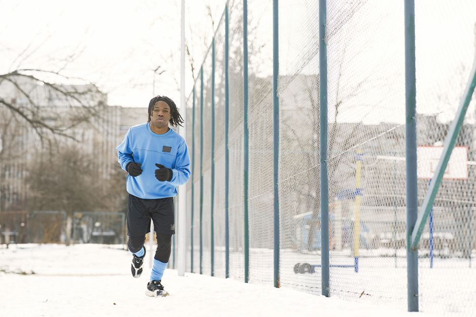 An adult man jogging on a snowy path beside a fence, embracing a healthy lifestyle in winter.