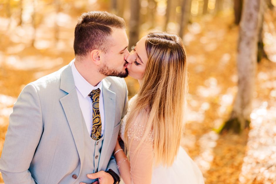 A couple shares a kiss in a vibrant autumn forest on their wedding day in Brașov, Romania.