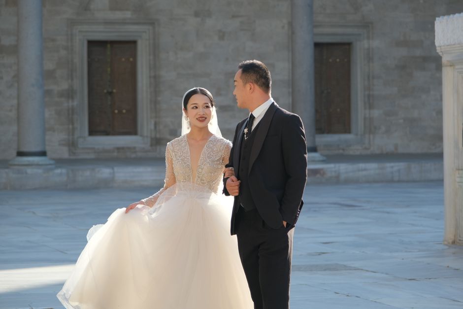 Bride and groom walking in a sunlit courtyard, expressing love and joy on their wedding day.